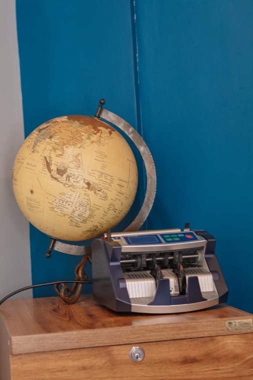 Globo terráqueo y contadora de billetes sobre un mueble de madera